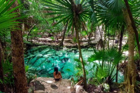 Mexique - Les Cenotes - Vue d'un centote bleu au centre d'une végétation luxuriante et jeune femme de dos observant le paysage